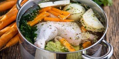 Stainless steel pot filled with chicken leg, carrots, onions and fresh herbs and water.